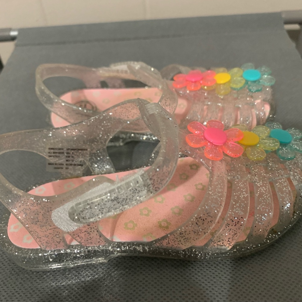 Clear with glitter closed toe sandles with three flowers on top. Size 5 kids.